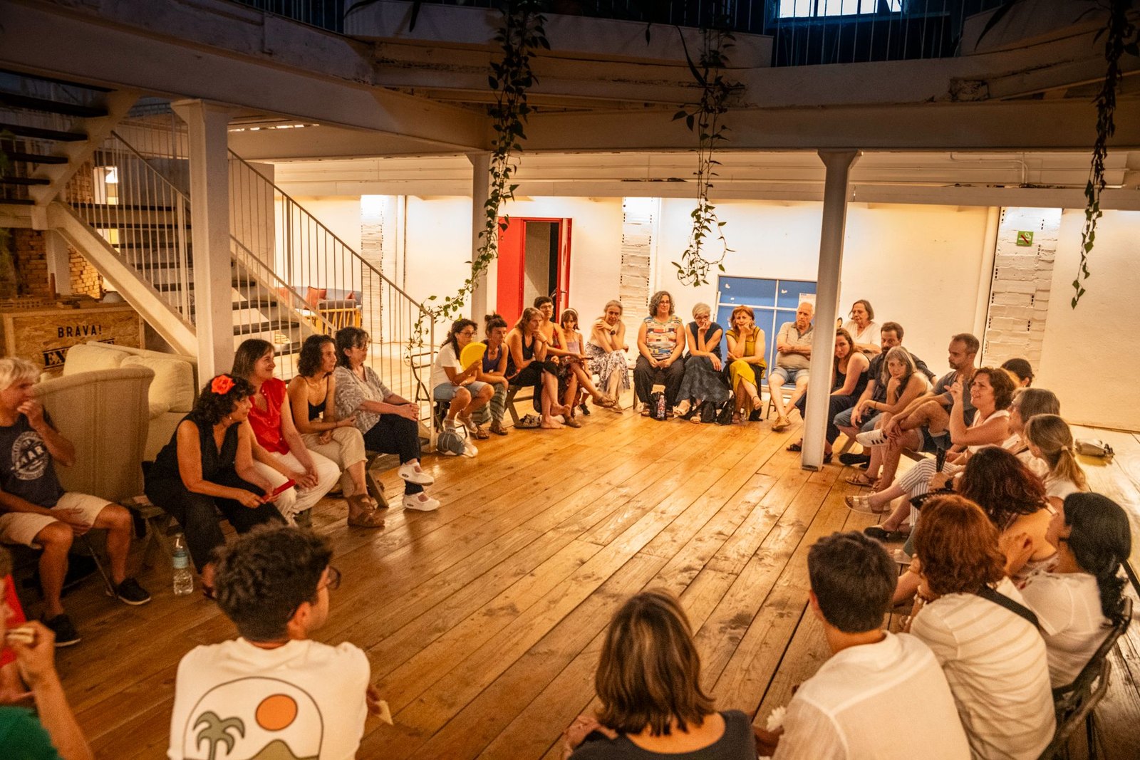 Participants and audience seated in a large circle in a warmly lit hall
