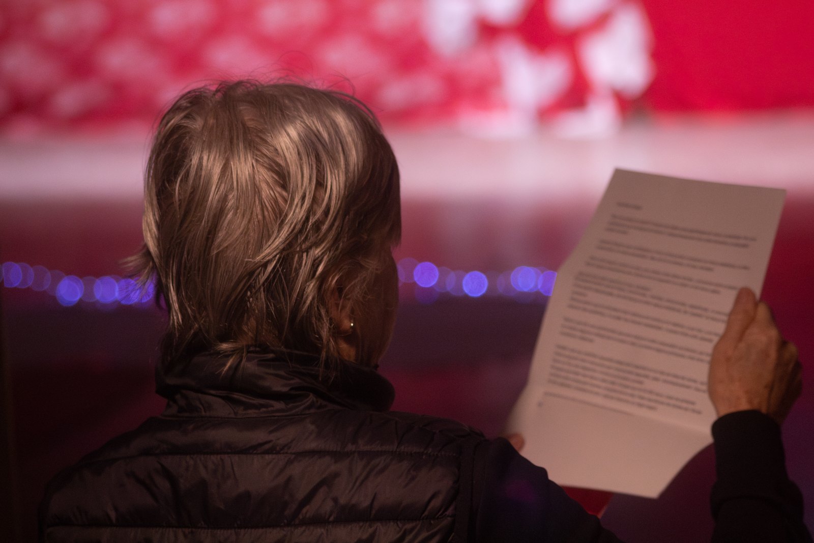 A member of the audience reading a printed text, with red projected light behind